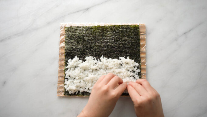 evenly spreading out rice on bottom half of nori