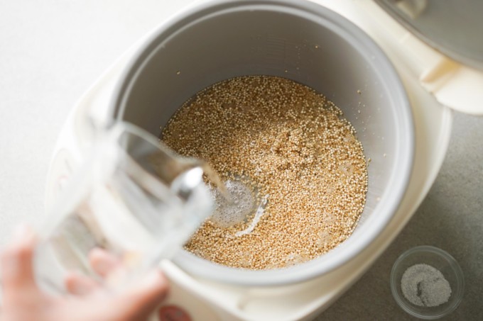 pouring water into rice cooker with raw quinoa