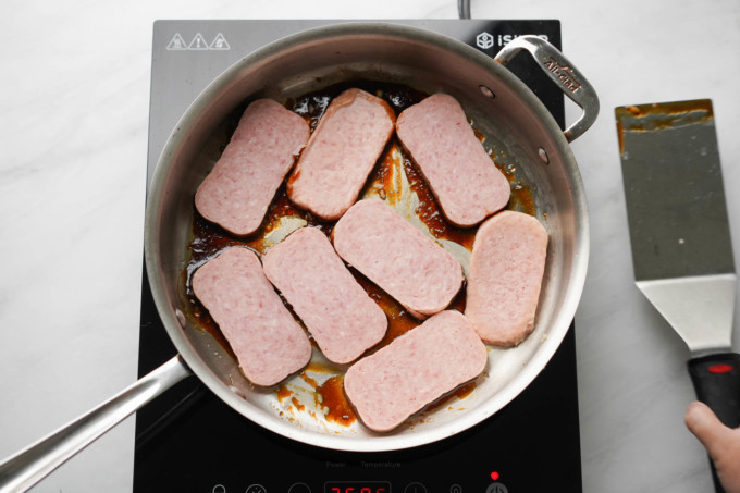 uncooked Spam slices in sauced pan