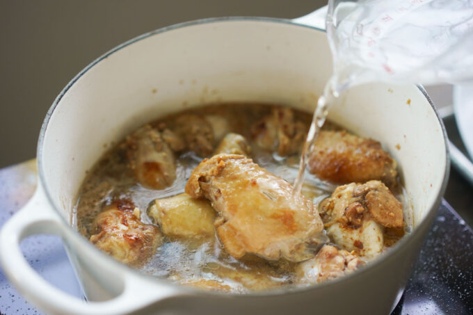 pouring water into pot of chicken adobo