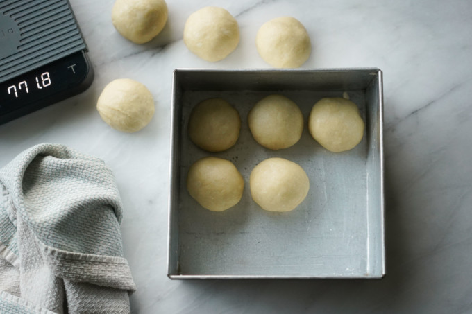 adding weighed dough balls into a buttered pan