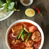 a bowl of bun rieu soup with veggies and herbs