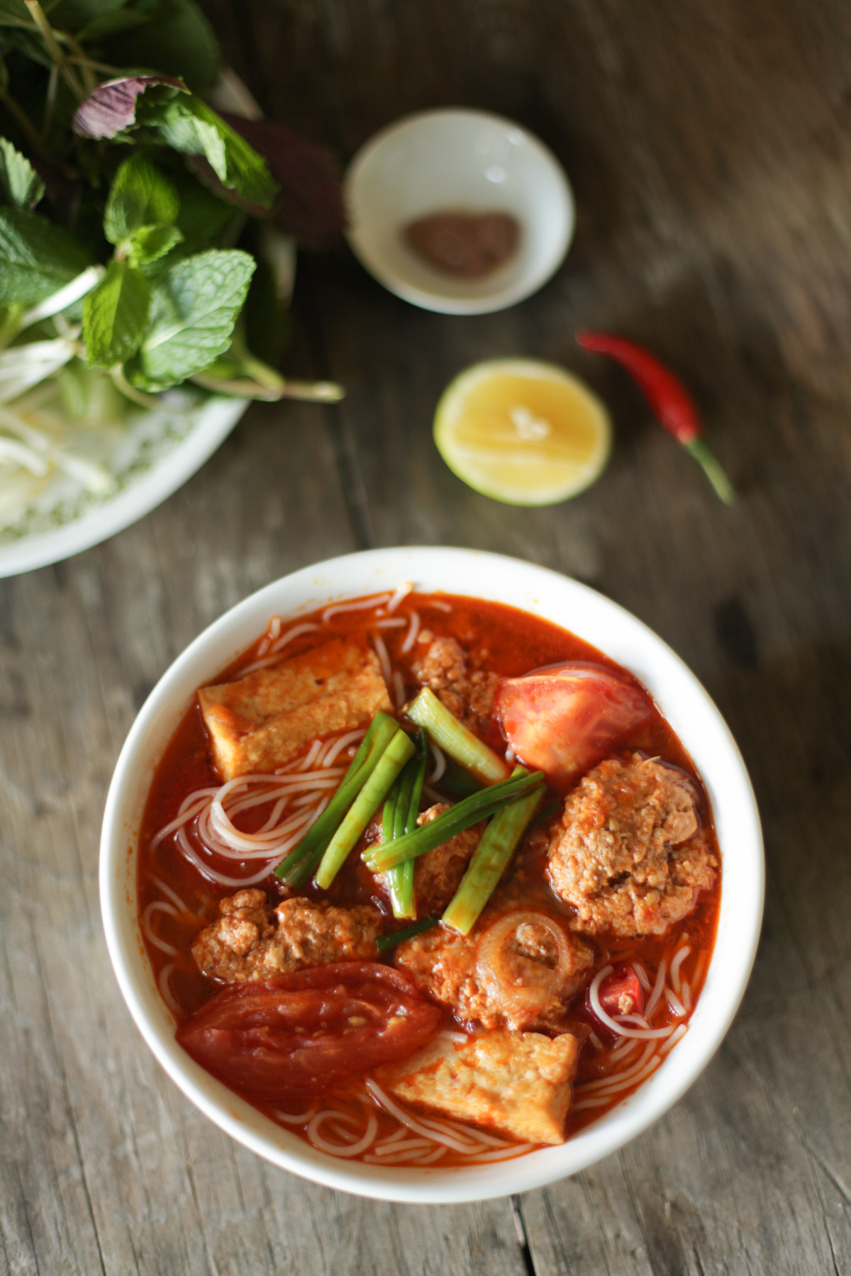 a bowl of bun rieu soup with veggies and herbs