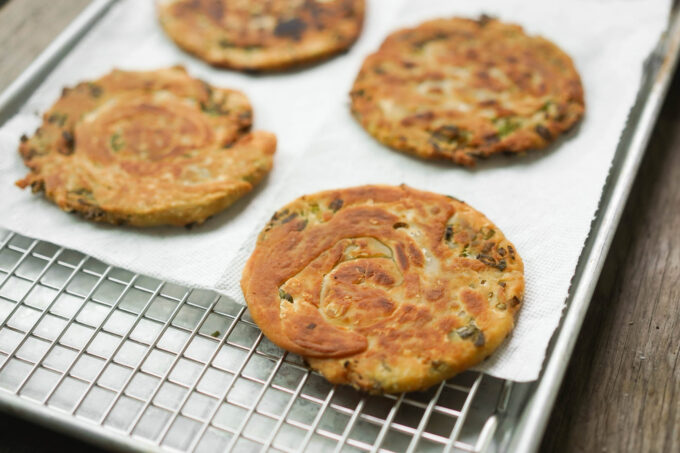 scallion pancakes draining on paper towel and cooling rack