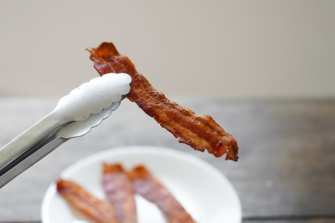 tongs holding up crispy bacon slice