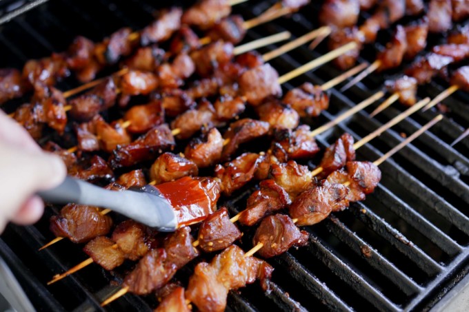 skewers of pork on the grill, being glazed with a brush
