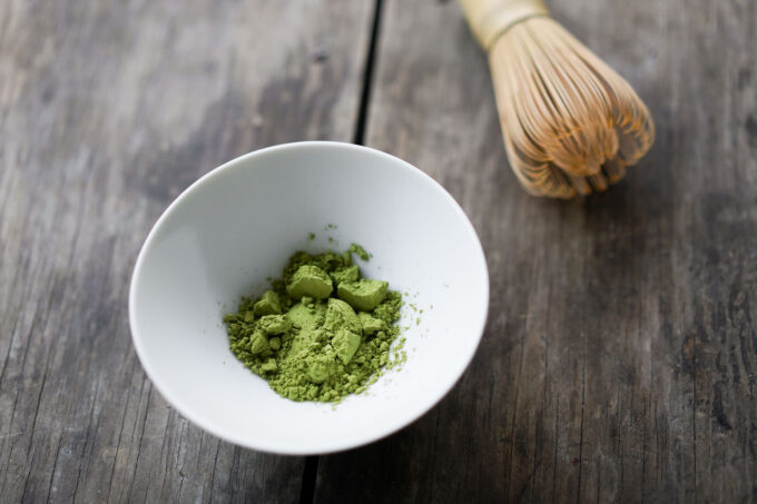 matcha powder in a bowl, next to a matcha whisk