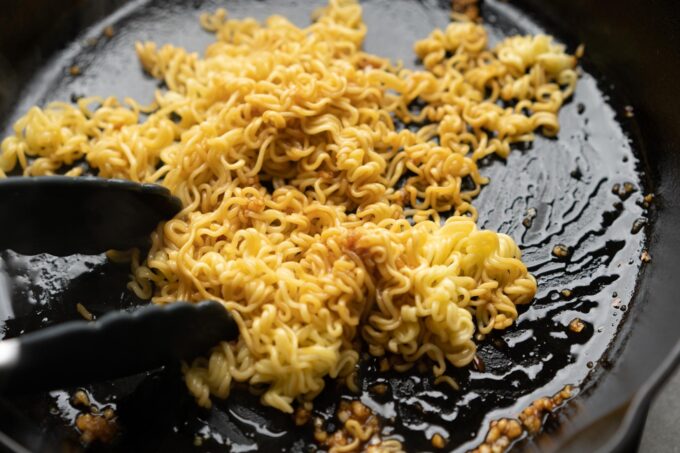 mixing cooked ramen noodles in sauce