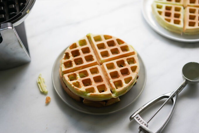 plate of pandan waffles next to waffle iron and scooper