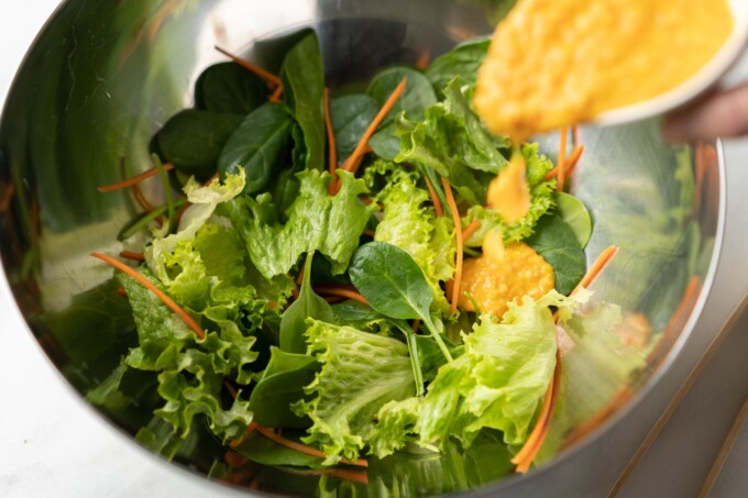 pouring asian ginger carrot dressing on greens