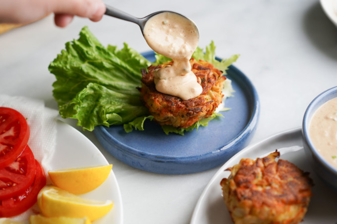 adding spoonful of sauce to a crab cake