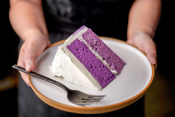 holding slice of ube cake on a plate