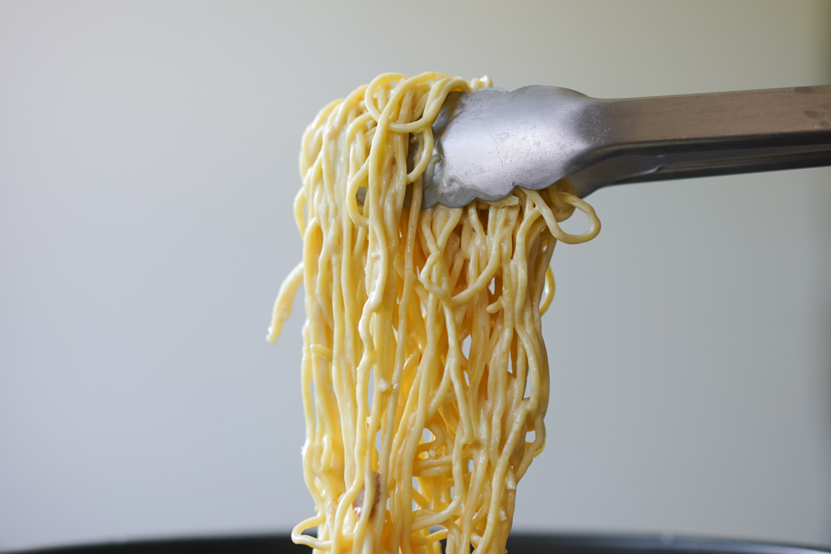 lifting creamy pasta with metal tongs