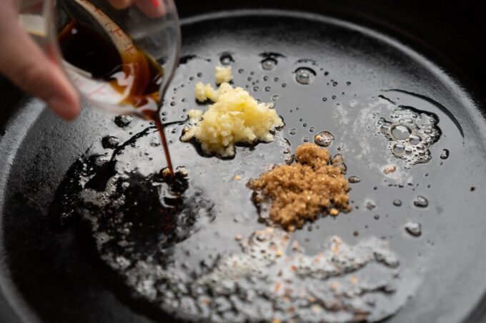 adding seasoning ingredients to cast iron pan