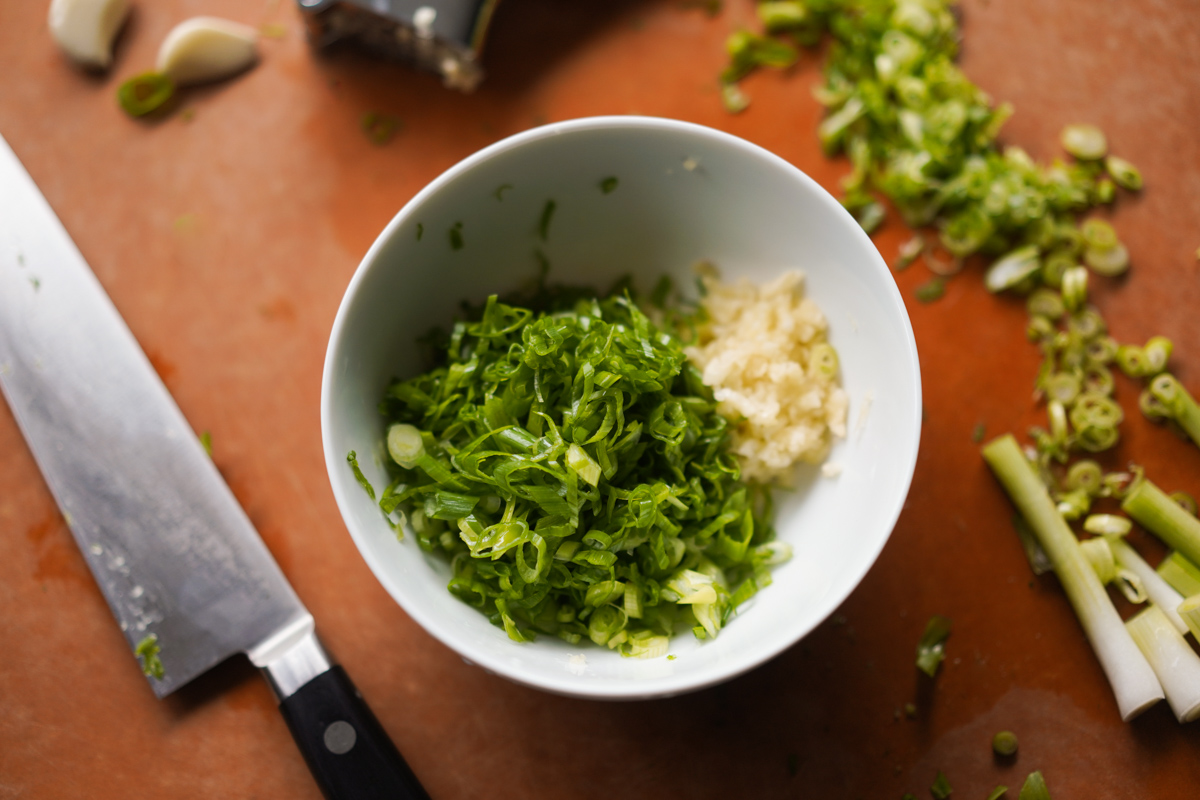 sliced scallions and pressed garlic on a cutting board