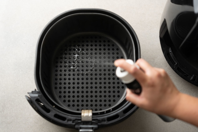 spraying air fryer basket with oil