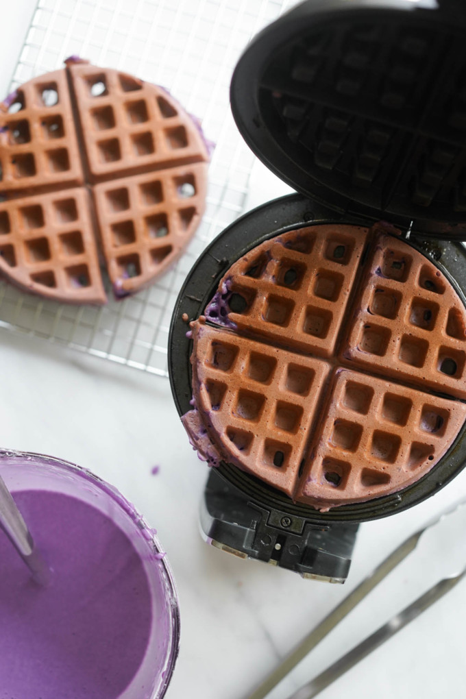 two baked ube waffles, one cooling, one in the iron